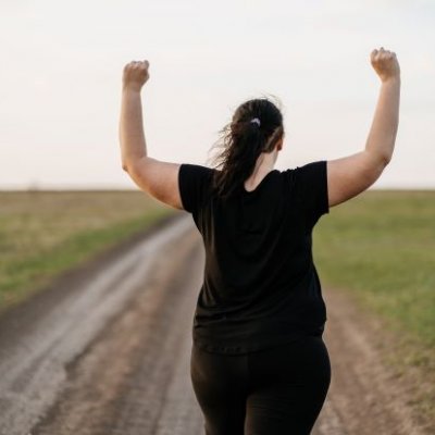 A woman with her back to the camera standing with a field with her arms raised 